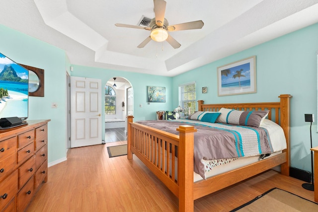 bedroom featuring a tray ceiling, multiple windows, ceiling fan, and light wood-type flooring