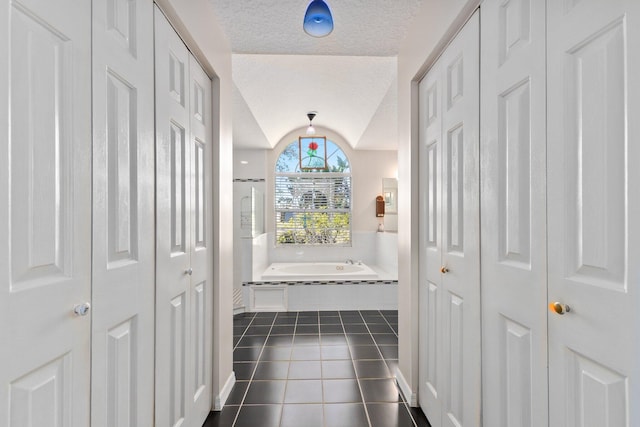 hall featuring a textured ceiling, dark tile patterned flooring, and lofted ceiling