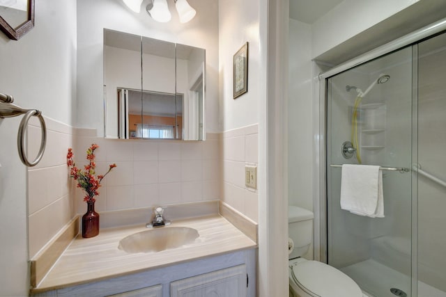 bathroom with toilet, vanity, tile walls, and a shower with shower door