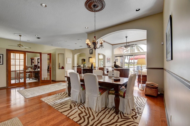 dining space featuring a textured ceiling, ceiling fan with notable chandelier, and light wood-type flooring