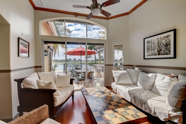 living room with ceiling fan, crown molding, wood-type flooring, and a high ceiling