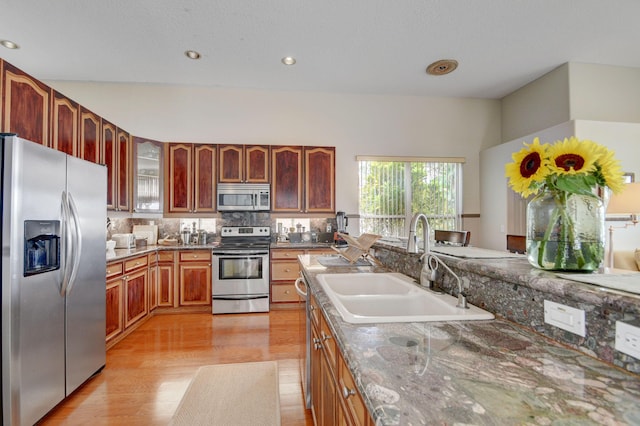 kitchen with decorative backsplash, dark stone counters, stainless steel appliances, sink, and light hardwood / wood-style floors