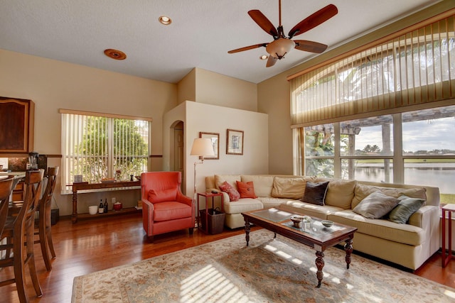 living room with ceiling fan, a water view, and dark wood-type flooring