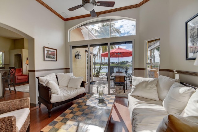 living room with a high ceiling, ceiling fan, crown molding, and wood-type flooring