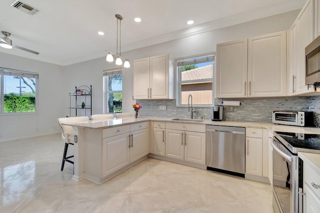 kitchen with sink, hanging light fixtures, kitchen peninsula, a breakfast bar, and appliances with stainless steel finishes