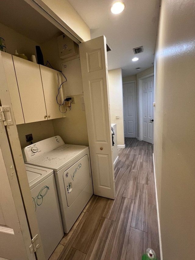 clothes washing area with cabinets, washer and dryer, and light hardwood / wood-style flooring