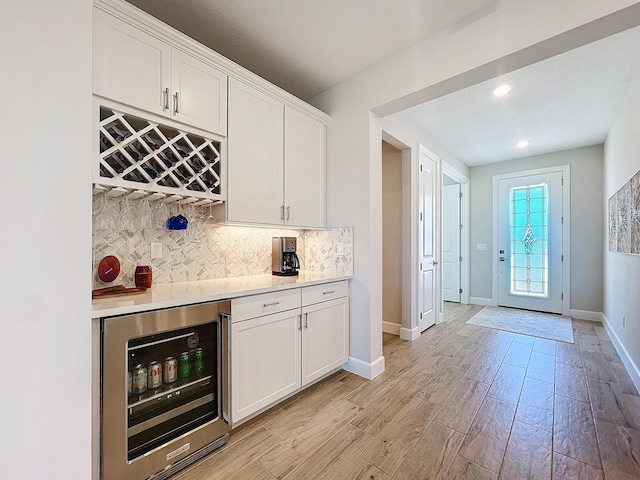 bar with white cabinets, wine cooler, light hardwood / wood-style floors, and decorative backsplash