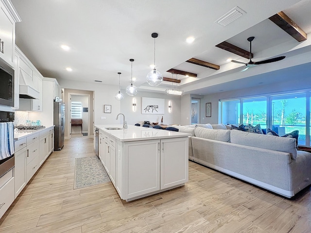 kitchen with appliances with stainless steel finishes, sink, white cabinets, a kitchen island with sink, and beam ceiling