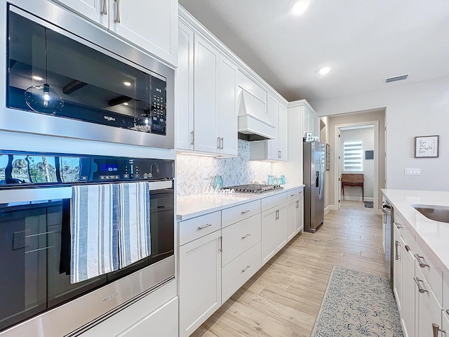 kitchen featuring white cabinetry, backsplash, custom range hood, and appliances with stainless steel finishes