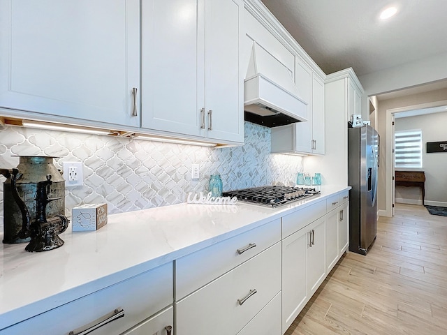 kitchen featuring premium range hood, appliances with stainless steel finishes, light stone countertops, decorative backsplash, and white cabinets