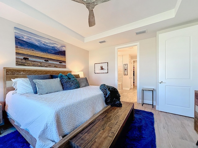 bedroom with ceiling fan, ensuite bath, a raised ceiling, and light hardwood / wood-style flooring