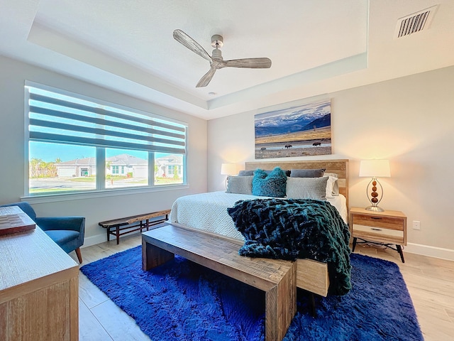 bedroom featuring light hardwood / wood-style floors, ceiling fan, and a tray ceiling