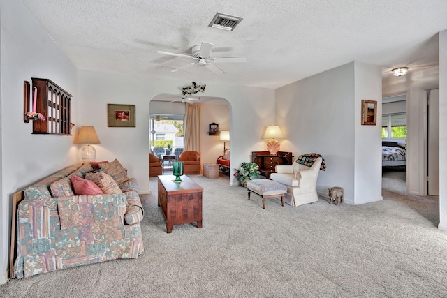 living room with a textured ceiling, light colored carpet, and ceiling fan