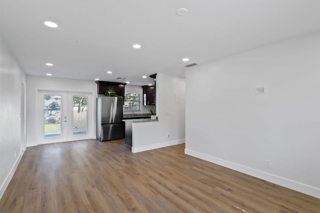 kitchen featuring dark brown cabinets, stainless steel fridge, dark hardwood / wood-style flooring, french doors, and light stone counters