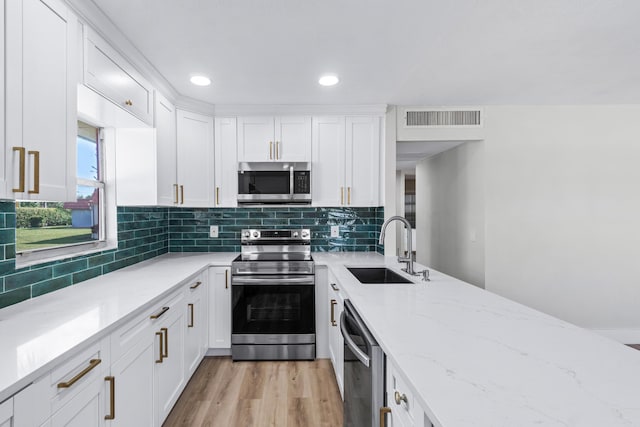 kitchen featuring stainless steel appliances, sink, white cabinets, light stone counters, and tasteful backsplash