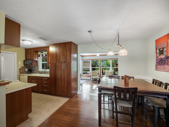 interior space featuring white appliances, backsplash, light wood-type flooring, a textured ceiling, and decorative light fixtures