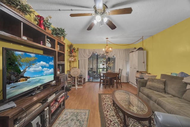 living room featuring wood-type flooring, ceiling fan with notable chandelier, and a textured ceiling