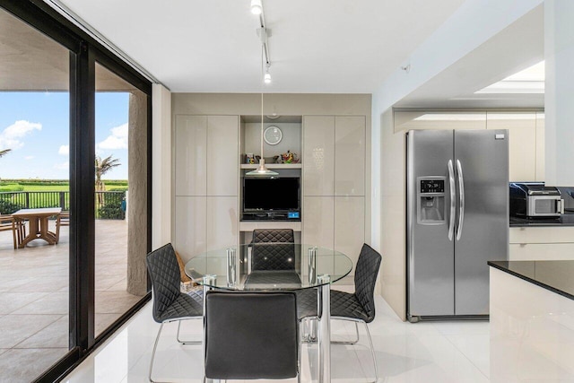 kitchen featuring stainless steel fridge with ice dispenser, light tile patterned floors, track lighting, white cabinets, and expansive windows