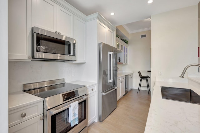 kitchen featuring light stone countertops, white cabinetry, sink, appliances with stainless steel finishes, and ornamental molding