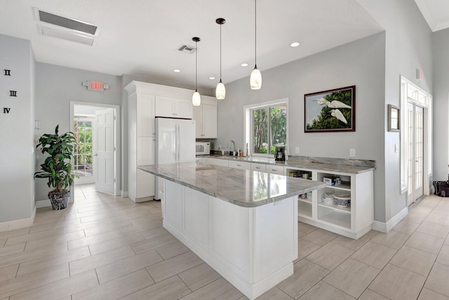 kitchen with white cabinetry, a center island, light stone countertops, decorative light fixtures, and white appliances