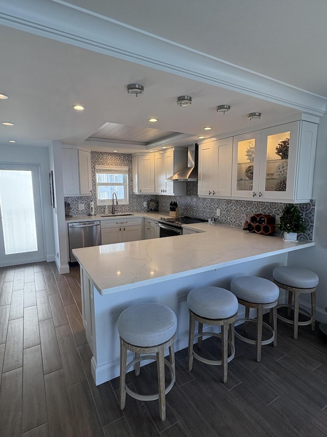 kitchen featuring wall chimney exhaust hood, white cabinetry, stainless steel appliances, and kitchen peninsula