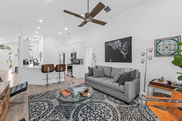 living room featuring ceiling fan, sink, high vaulted ceiling, and light wood-type flooring