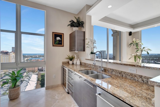 kitchen with a tray ceiling, light stone countertops, sink, and dishwasher