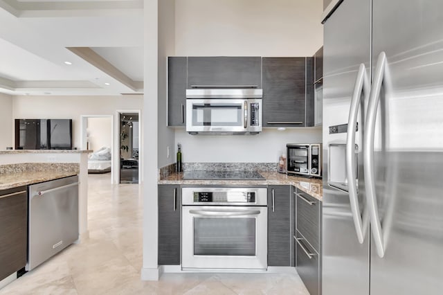 kitchen featuring a raised ceiling, light stone counters, dark brown cabinetry, and appliances with stainless steel finishes