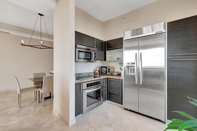 kitchen featuring light stone countertops, appliances with stainless steel finishes, dark brown cabinets, pendant lighting, and a notable chandelier