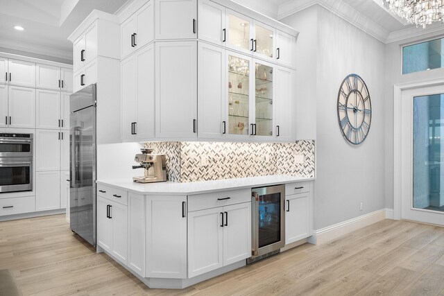 kitchen with decorative backsplash, white cabinetry, high end appliances, and wall chimney range hood