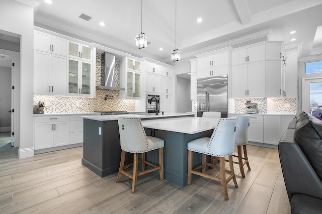 kitchen with white cabinets, built in refrigerator, a kitchen island with sink, and wall chimney range hood