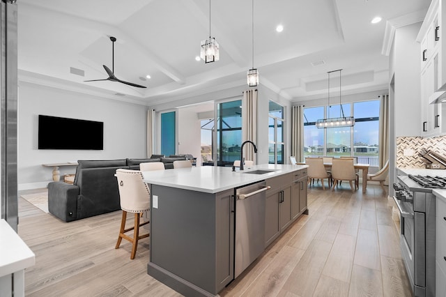 kitchen with appliances with stainless steel finishes, white cabinetry, sink, hanging light fixtures, and a center island with sink