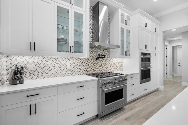 kitchen with light hardwood / wood-style flooring, appliances with stainless steel finishes, white cabinetry, backsplash, and wall chimney exhaust hood