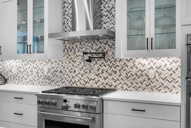 kitchen with tasteful backsplash, white cabinets, high end stainless steel range, and wall chimney exhaust hood