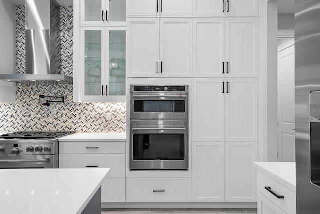 kitchen featuring appliances with stainless steel finishes, wall chimney range hood, white cabinets, and decorative backsplash