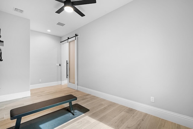 exercise room with ceiling fan, wood-type flooring, and a barn door