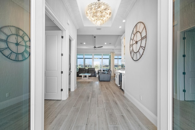 hall featuring a notable chandelier, ornamental molding, a raised ceiling, and light wood-type flooring