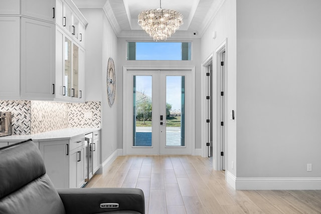 foyer featuring ornamental molding, a tray ceiling, light wood-type flooring, and french doors