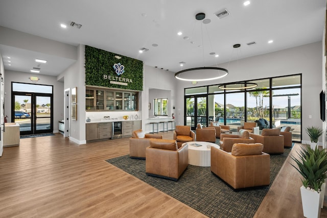 living room featuring a healthy amount of sunlight, a towering ceiling, hardwood / wood-style floors, and beverage cooler