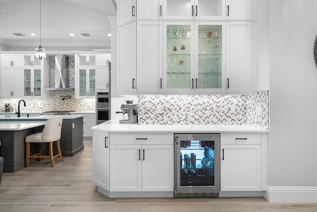 bar with sink, pendant lighting, wall chimney range hood, beverage cooler, and white cabinets