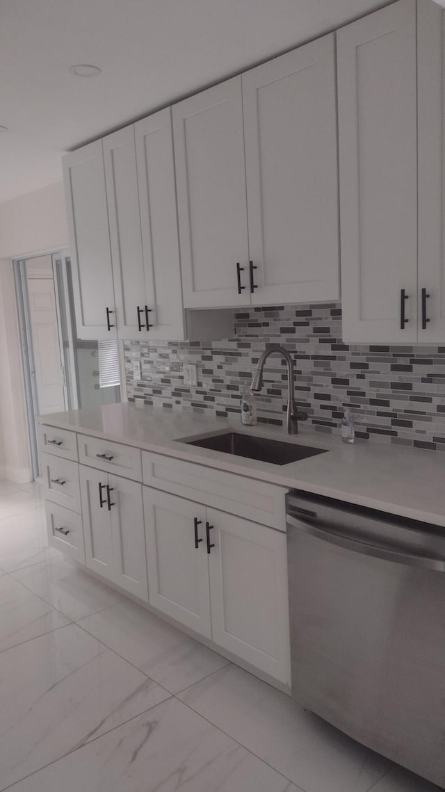 kitchen featuring stainless steel dishwasher, white cabinetry, sink, and tasteful backsplash