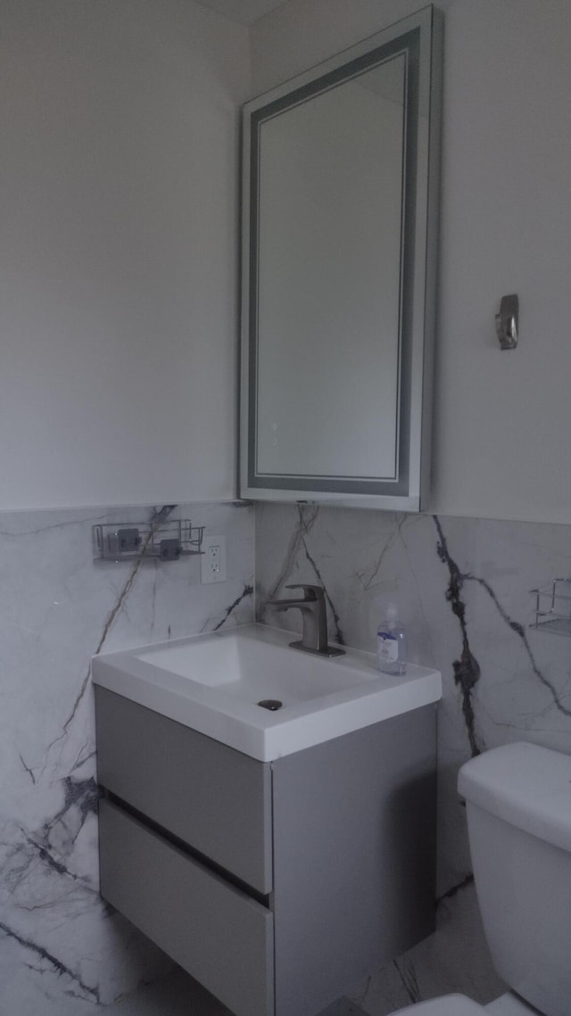 bathroom featuring vanity, toilet, and tile walls