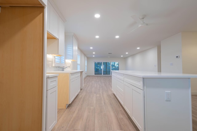 kitchen with a center island, white cabinets, light hardwood / wood-style flooring, ceiling fan, and tasteful backsplash