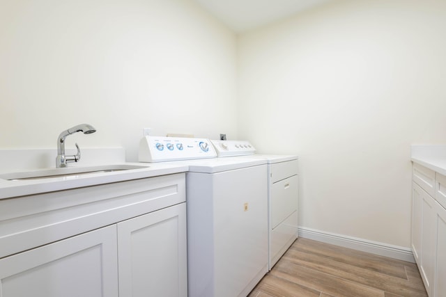 clothes washing area featuring washer and dryer, light hardwood / wood-style floors, cabinets, and sink