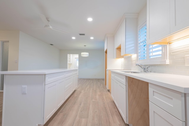 kitchen with backsplash, white cabinets, sink, light hardwood / wood-style flooring, and decorative light fixtures