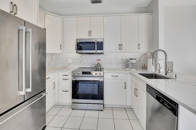 kitchen with white cabinets, sink, light tile patterned floors, light stone counters, and stainless steel appliances