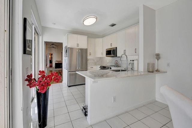 kitchen featuring kitchen peninsula, appliances with stainless steel finishes, decorative backsplash, sink, and white cabinets