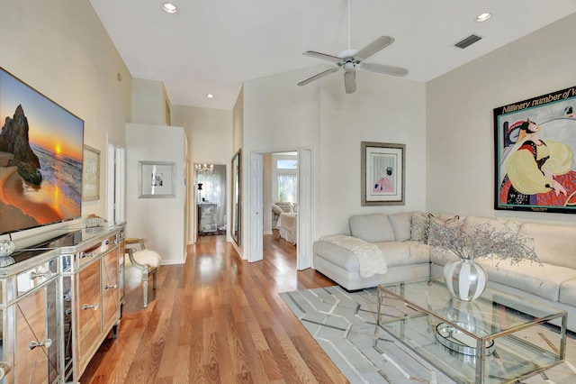 living room with ceiling fan, a high ceiling, and light hardwood / wood-style flooring