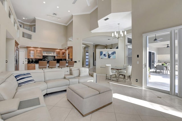 tiled living room featuring ceiling fan with notable chandelier, rail lighting, crown molding, and a high ceiling