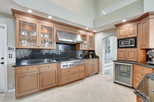 kitchen featuring appliances with stainless steel finishes, beverage cooler, dark stone counters, and wall chimney exhaust hood